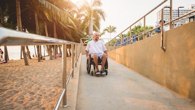 Disabled man in a wheelchair moves on a ramp to the beach.