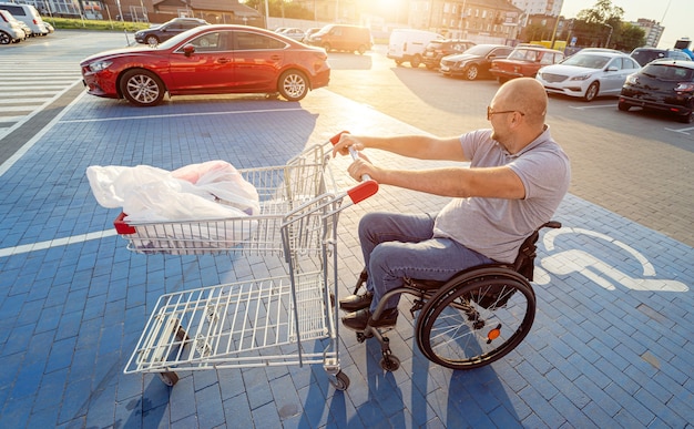 スーパーマーケットの駐車場で自分の前にカートを押す車椅子の障害者の男性