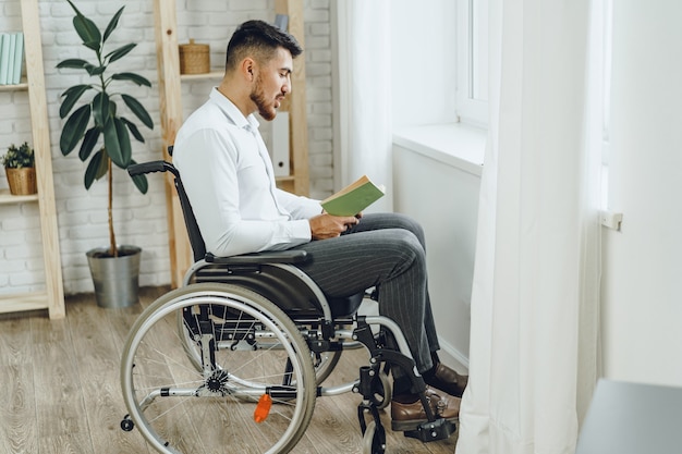 Uomo disabile in sedia a rotelle leggendo un libro al chiuso