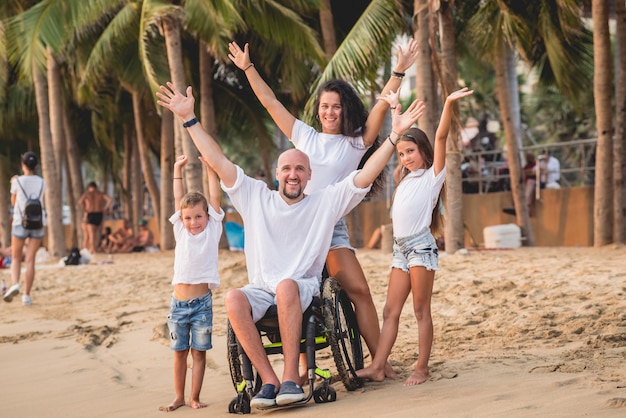 Disabled man in a wheelchair with his family on the beach.