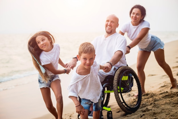 Инвалид человек в инвалидной коляске со своей семьей на пляже.