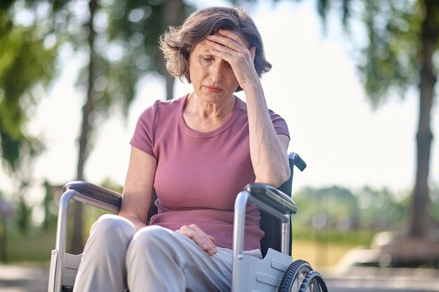 Donna di mezza età disabile seduta su una sedia a rotelle con uno sguardo infelice
