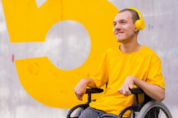 Disabled person dressed in yellow in a wheelchair smiling listening to music