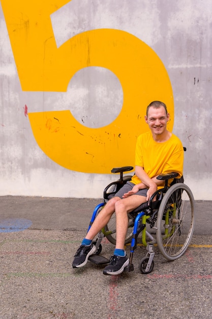 Фото Инвалид в общественном парке в инвалидной коляске в желтой футболке улыбается