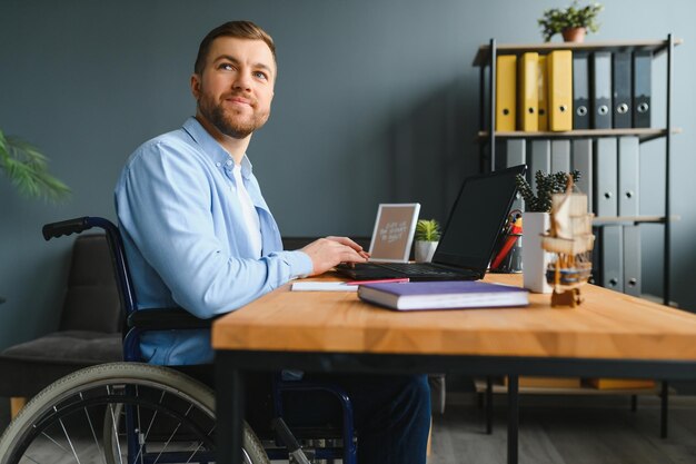 Disabled person in the wheelchair works in the office at the computer He is smiling and passionate about the workflow