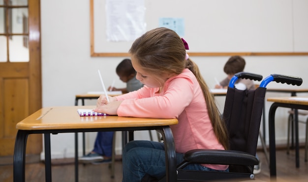 Disabled pupil writing at desk in classroom