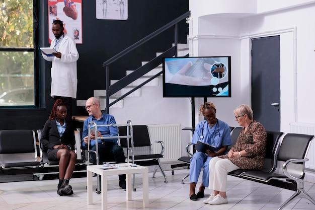 Disabled senior patient with walking frame sitting in hospital reception discussing medical insurance with receptionist during checkup visit appointment. Health care service and concept