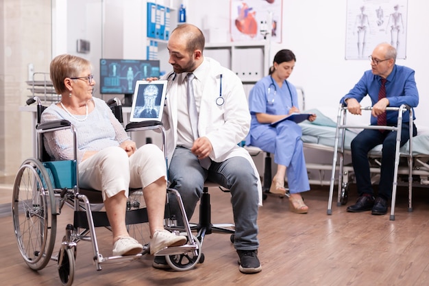 Donna anziana disabile con disabilità motoria seduta in sedia a rotelle che parla con il medico utilizzando un tablet pc