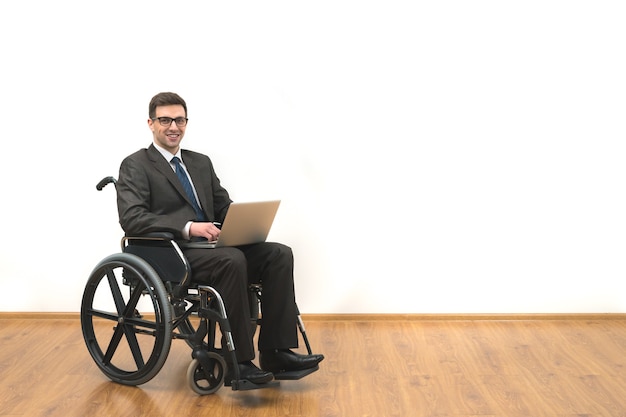 The disabled in a wheelchair works with a laptop on a white wall background