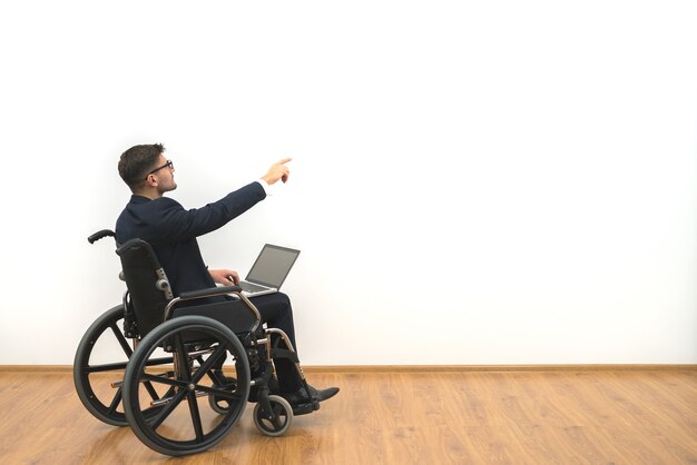 The disabled with a laptop gesturing on the white wall background