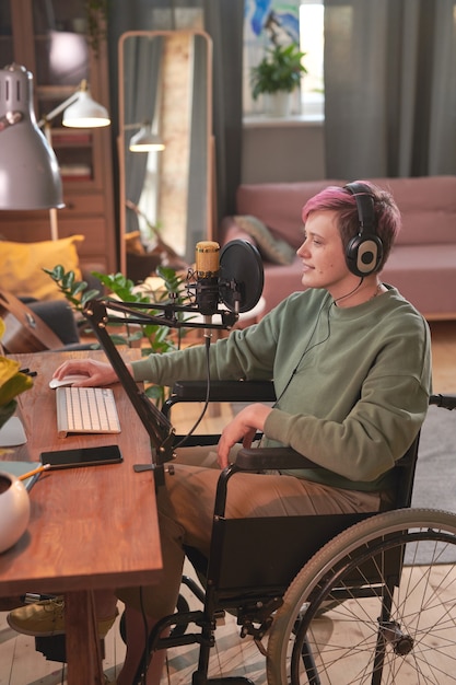 Disabled woman in headphones sitting at the table in front of computer and singing she recording her song at home