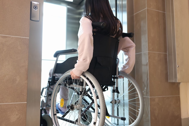 Disabled woman in wheelchair entering elevator back view