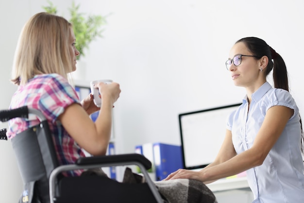 Disabled woman in wheelchair is drinking tea and talking with psychologist