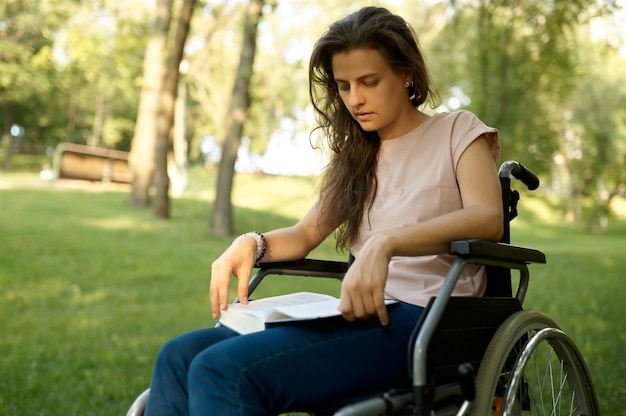 Donna disabile in sedia a rotelle che legge libro nel parco