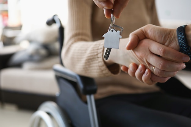 Disabled woman in wheelchair shaking hands with man with keys to new apartment closeup