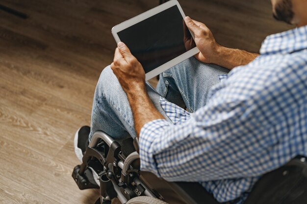 Disabled young african american man sitting in wheelchair and using digital tablet