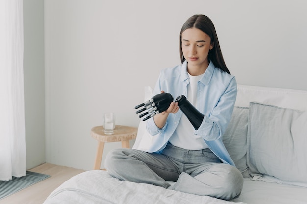 Disabled young girl disassembles bionic prosthetic arm sitting on bed at home Medical technologies