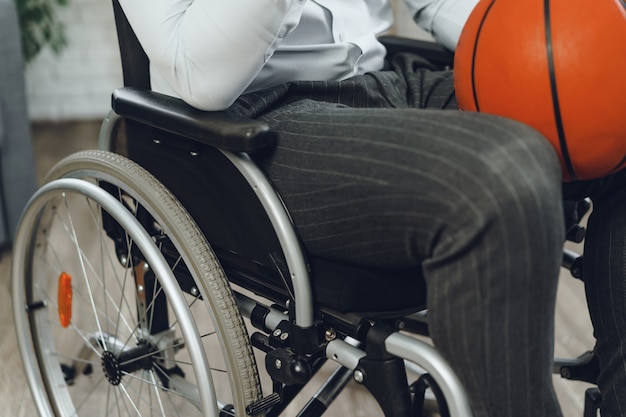 Disabled young man in wheelchair holding basketball ball indoors