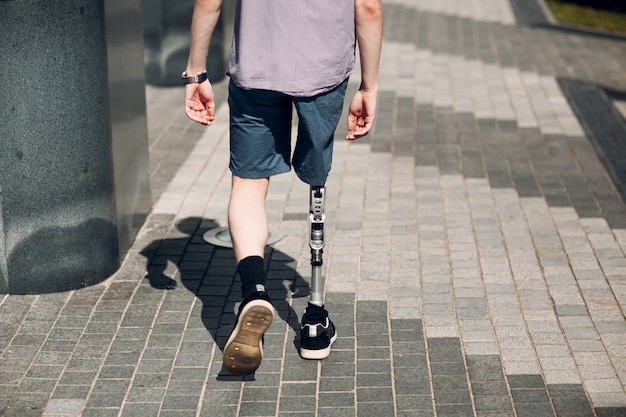 Disabled young man with foot prosthesis walks along the street.