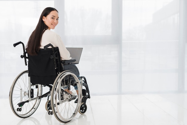 Foto giovane donna invalida che per mezzo del computer portatile che osserva sopra la spalla