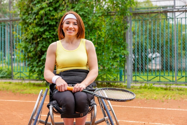 Photo disabled young woman on wheelchair playing tennis on tennis court.