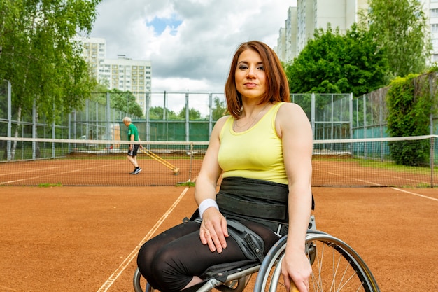 Неработающая молодая женщина на кресло-коляске играя теннис на теннисном корте.