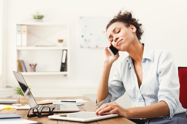 Disappointed african-american woman talking on phone at modern office copy space. Business consulting.