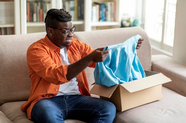 Disappointed african american young guy customer opening parcel checking good