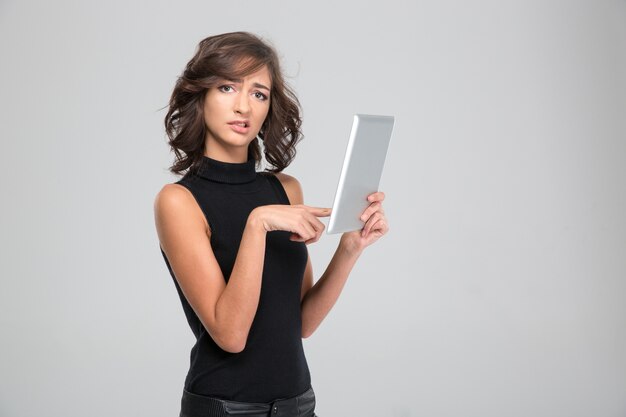 Disappointed annoyed young woman in black clothes using tablet