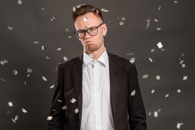 Disappointed birthday guy Boring party Annoyed business man alone in confetti rain isolated on dark Ruined celebration Holiday melancholy Quarantine crisis