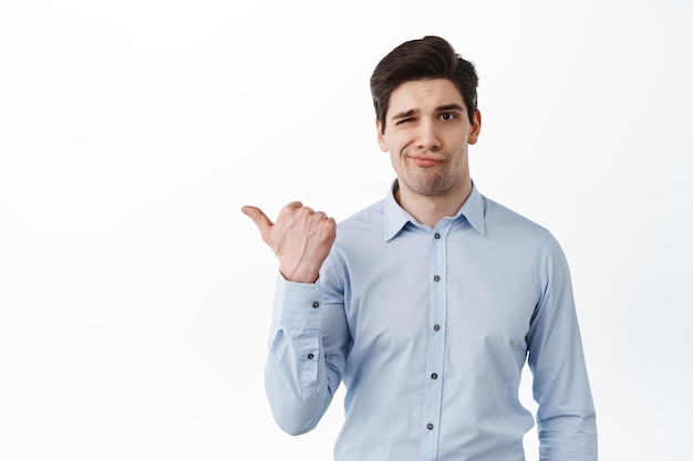 Disappointed corporate man, office worker frowning and say no, pointing left at something bad, look doubtful and displeased, standing over white background