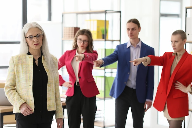 Disappointed employees point fingers to mature staff member standing in company office angry