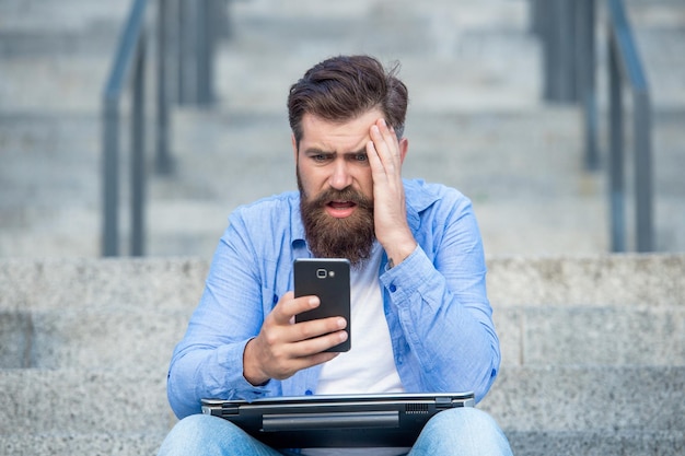 Photo disappointed guy lost bet upset guy checking up betting results in mobile phone making bet