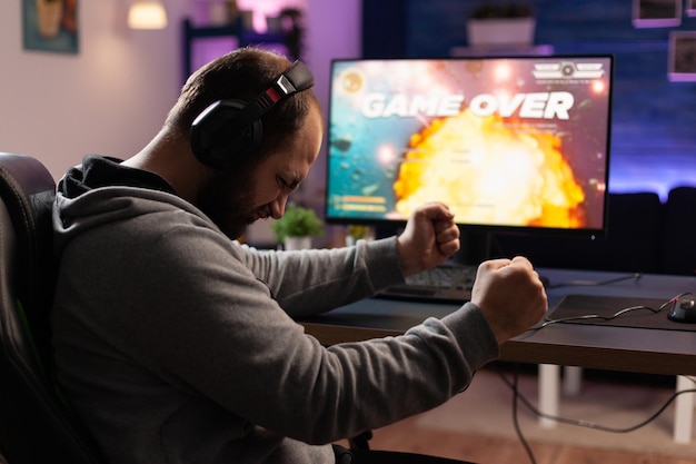 Disappointed man losing video games on computer. adult\
clenching fists and playing games with headphones and joystick,\
feeling sad about lost game. player using modern equipment.