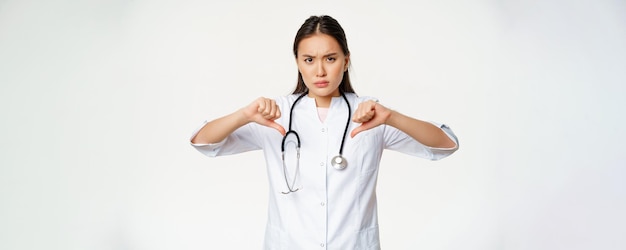 Disappointed seriouslooking asian female doctor hospital physician shows thumbs down with disapprova