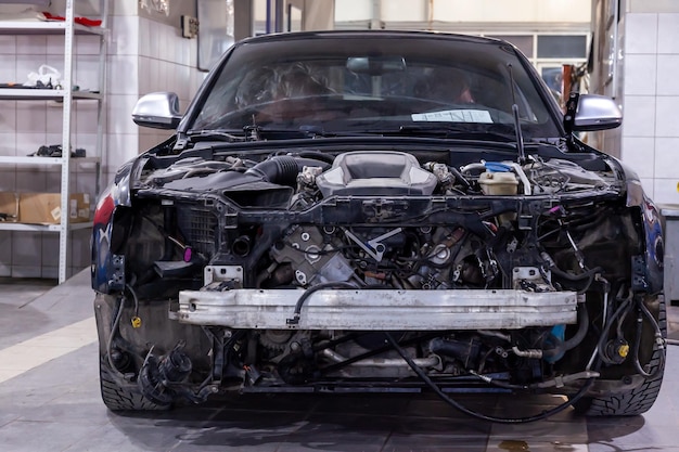Disassembled black car in the workshop prepared for repair front end hood and bumper removed internal equipment parts and spare parts visible