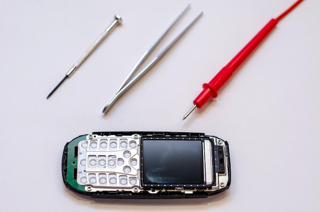 Disassembled mobile phone on the table of a mechanical engineer\
during repair tweezers and screwdriver for repairing electronic\
gadgets on a white background