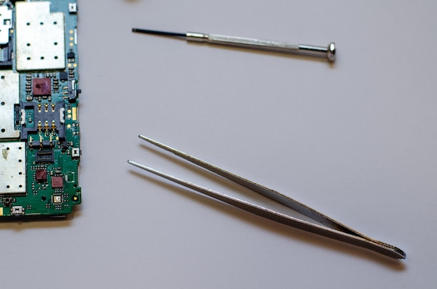 Disassembled mobile phone on the table of a mechanical engineer during repair Tweezers and screwdriver for repairing electronic gadgets on a white background