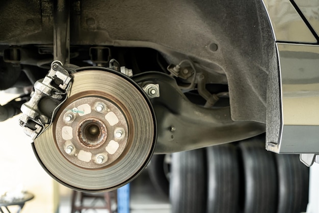 Foto primo piano dell'auto del disco - meccanico che svita le parti dell'automobile mentre lavora sotto un'auto sollevata - concetto di servizio dell'auto