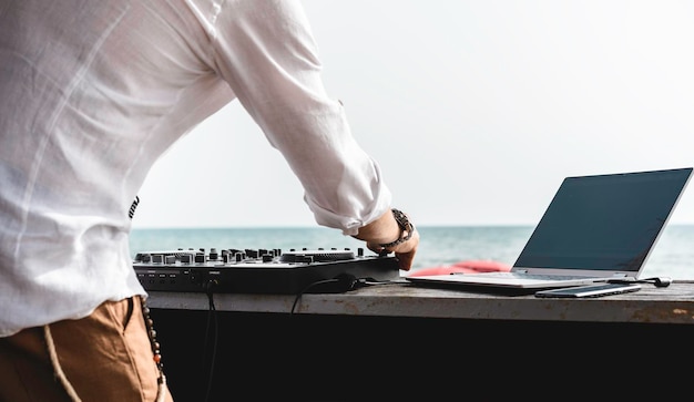 Disc jockey playing music for tourist people at club party outdoors on the beach Dj at music live event Live event music and fun concept Entertainment and party concept Focus on hands