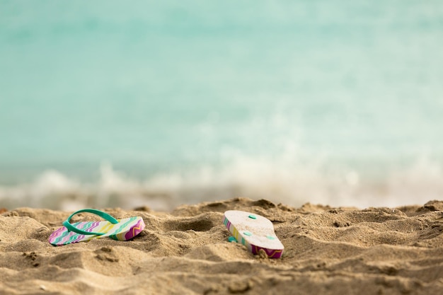 Discarded flipflops on sandy beach by ocean