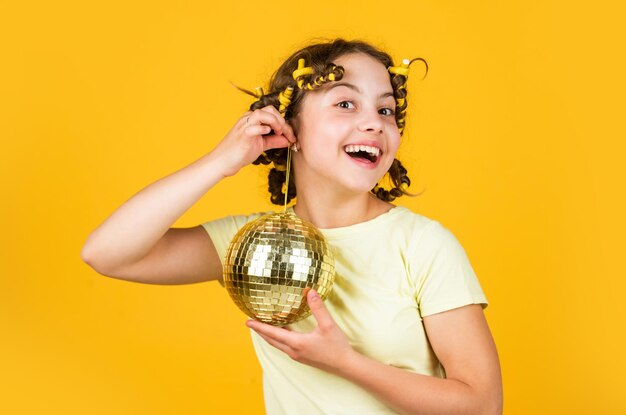 Photo disco ball decoration. lovely girl with disco ball. fashion girl posing in curlers on yellow wall. saturday night and disco ball. baby shower party. lets have fun on retro party. holiday objects.