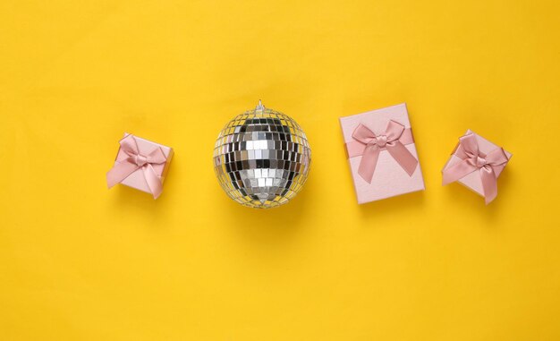 Photo disco ball and gift boxes on yellow background minimalism party and holiday concept