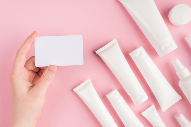 Discount card to shop online concept. Top above overhead pov first person view photo of female hand holding voucher isolated on pink pastel background with white cream tubes