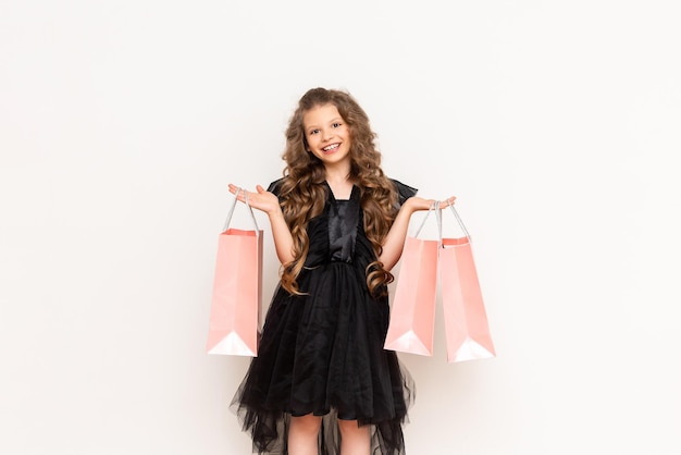 Discounts on Black Friday A little girl in a dress and curly hair holds shopping bags on a white isolated background Shopping for children Copy space