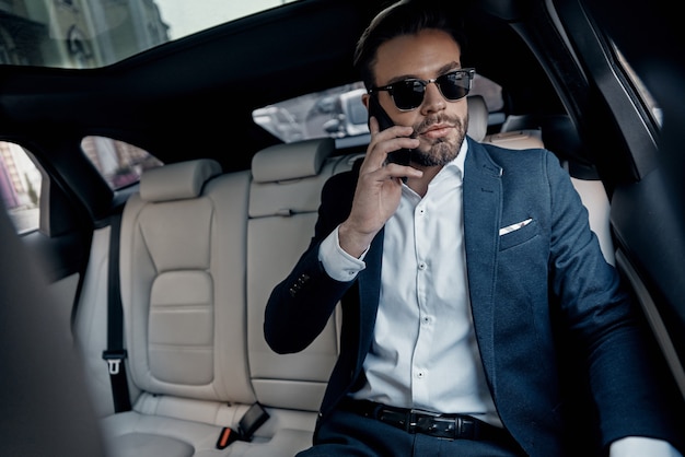 Photo discussing business details. handsome young man in full suit talking on his smart phone while sitting in the car