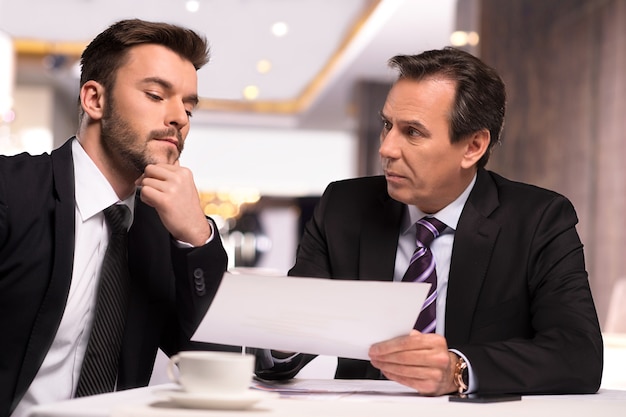 Discussing contract. Two business people in formalwear discussing something while one of them showing a paper to another one