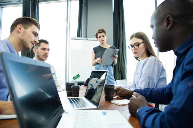 Discussing new business ideas. Cheerful young woman standing near whiteboard and smiling while her colleagues sitting at the desk.