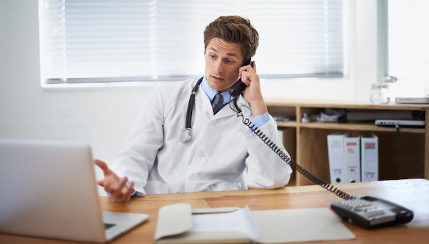 Foto discutere lo stato di un paziente inquadratura di un giovane medico seduto nel suo ufficio e parlando al telefono