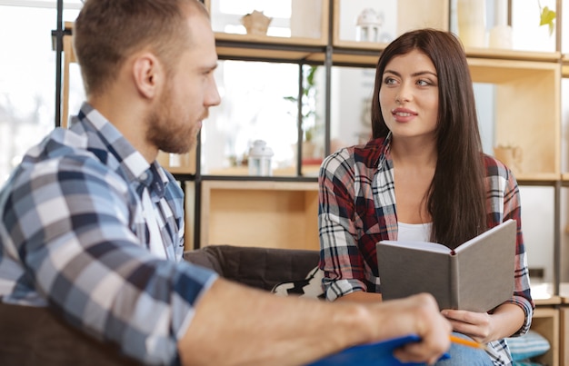 Discussing work. Delighted attractive brunette woman holding a notebook and looking at her colleague while discussing work issues with him